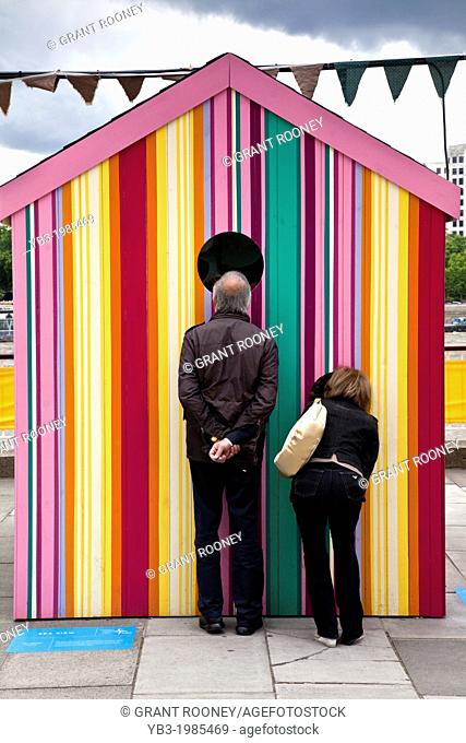 A couple look through the window of a beach hut, erected for the festival of Britain, The Southbank, London, England