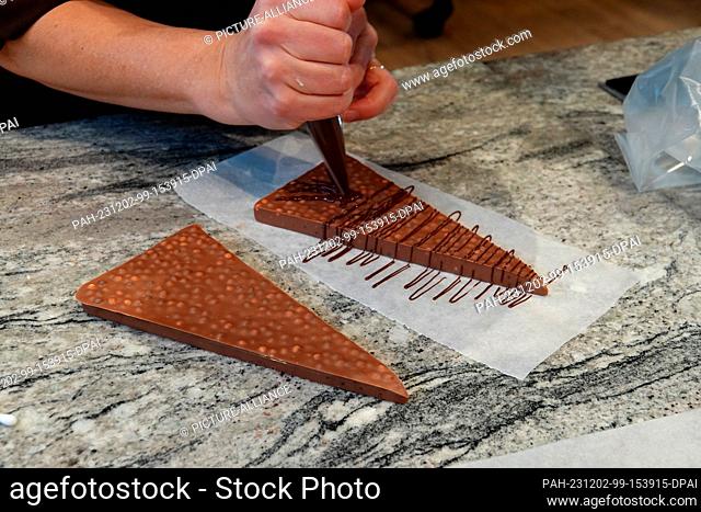 PRODUCTION - 13 November 2023, Switzerland, Broc: Chocolatière Géraldine Müller Maras decorates a homemade triangular chocolate bar with liquid chocolate in the...