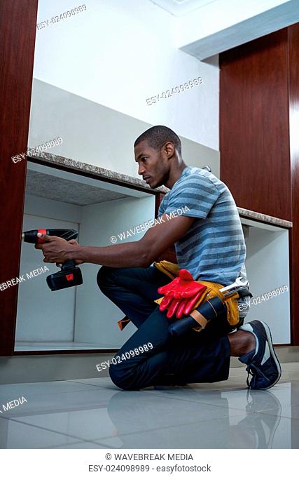 Manual worker drilling a hole in kitchen