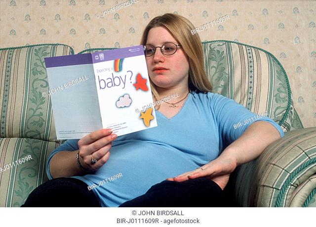 Pregnant teenage girl reading information leaflet about pregnancy
