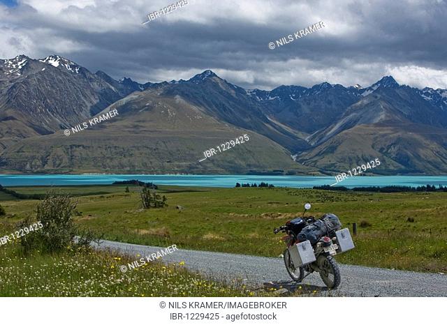 Enduro motorcycle on a gravel road at the glacial Lake Pukaki, with a view to the mountains of the Ben Ohau Range, South Island, New Zealand