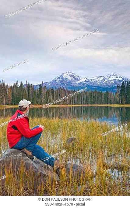 Man sitting on a rock at the lakeside, Scott Lake, Three Sisters, Willamette National Forest, Oregon, USA