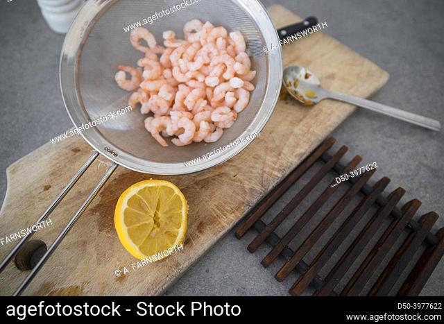 Rinsed small shrimp in a colander on a board with lemon