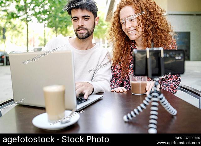 Boyfriend using laptop while sitting with girlfriend at outdoor cafe