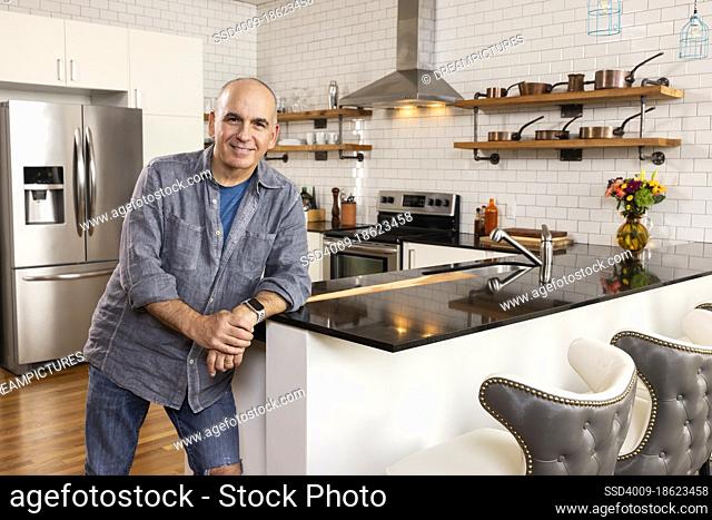 Caucasian man standing at the edge of kitchen looking into camera smiling