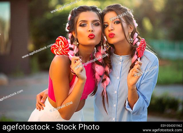 Two pretty and fashionable girls wearing in trendy clothes with colorful hair and professional makeup after shoping. Women making duckface and looking at camera