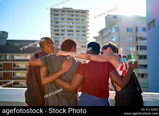 Young friends hugging on sunny urban rooftop balcony