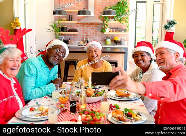 Diverse group of happy senior friends in holiday hats celebrating christmas together, taking selfie