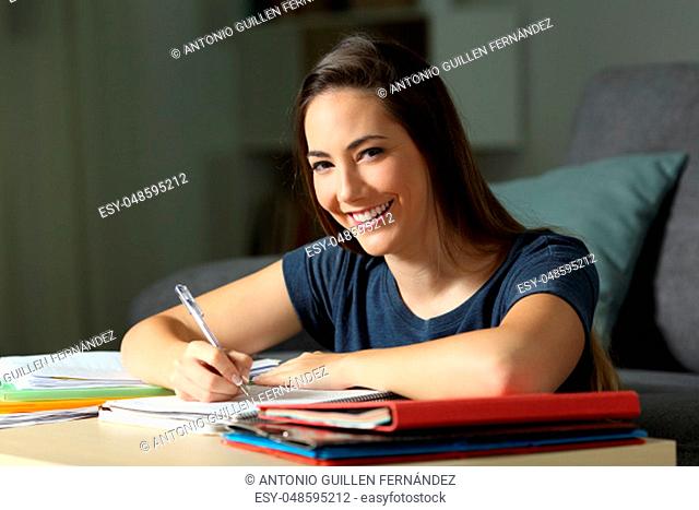 Happy student studying late hours in the night looking at you at home