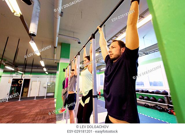 sport, fitness, exercising and training concept - group of people hanging at horizontal bar in gym