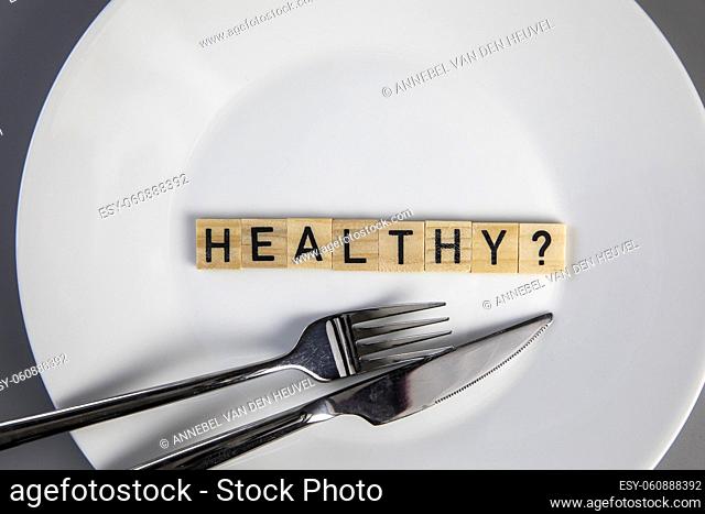 White plate with the words Healthy and a question mark top view with fork and knife, medical health and food concept background
