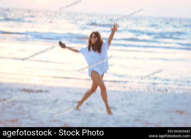 Photo in motion of a happy cheerful girl dancing on the beach. Having fun outdoors. Spending active summer weekend near the sea. Blur in motion