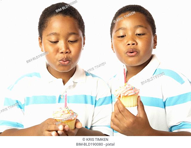 Young African twin brothers holding cupcakes with candles