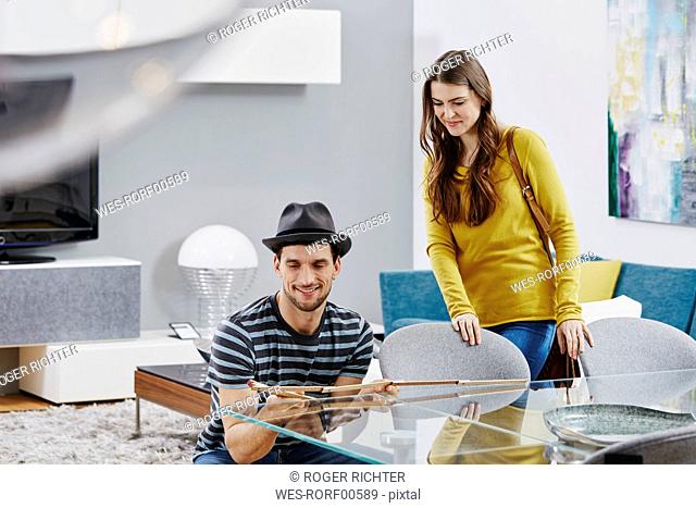 Couple in furniture store measuring dining table with pocket rule