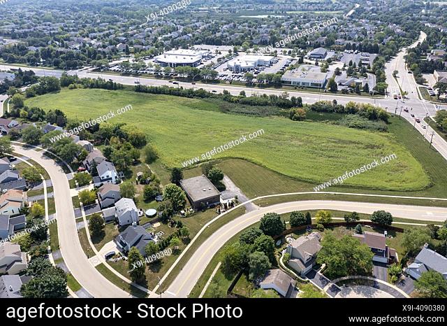 A aerial showing a parcel of land for sale near a housing development and retail shopping center in a suburban area