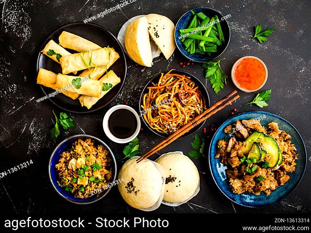 Asian assorted food set, dark rustic stone background. Chinese dishes. Chinese stir-fry noodles, asian rice with meat, dim sum, fried spring rolls