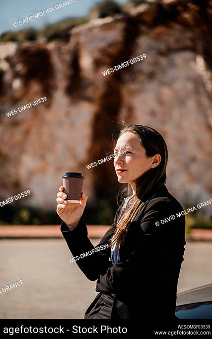 Thoughtful businesswoman looking away while holding disposable coffee cup on sunny day