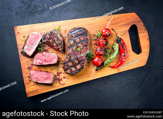 Barbecue dry aged wagyu roast beef steak with tomatoes and chili as top view on a modern design wooden board