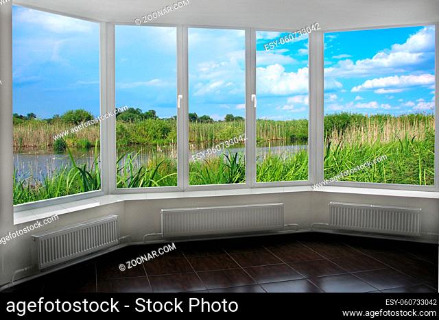 Room with wide window overlooking landscape with lake surrounded with cane. View from room window to brushwood of rush in lake