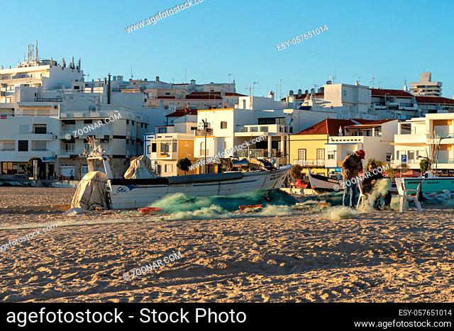 Amarcao da Pera, Portugal - 30 December 2020: fishermen on the Praia dos Pescadores mending and repairing their gear and nets