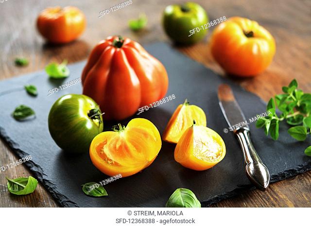 Colorful rustic tomatoes on cutting board with old knife and herbs