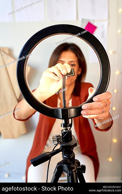 Female fashion designer adjusting circle light for vlogging at atelier