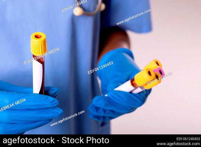 Midsection of african american mid adult female doctor wearing gloves holding test tubes with blood