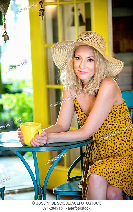 A pretty 30 year old blond woman sitting in a cafe holding a large cup of coffee smiling at the camera