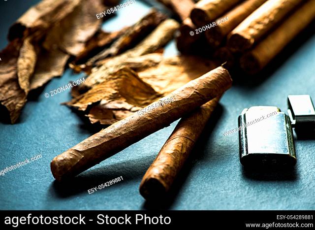 Cuban cigars with leafs and lighter on dark background