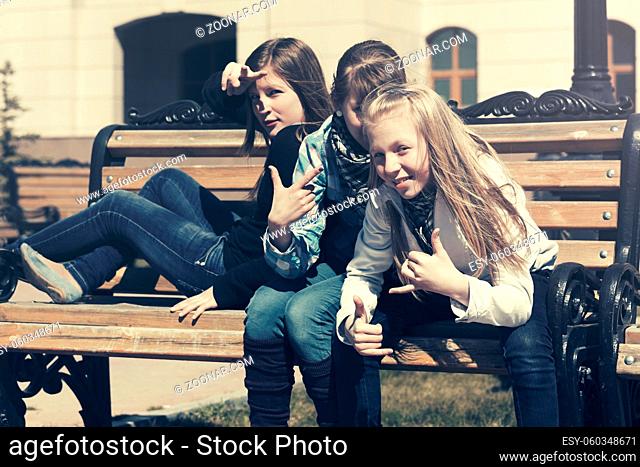 Group of happy teen girls sitting on bench in city street