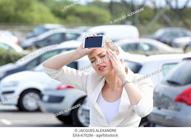 Woman in car park with mobile phone, headache