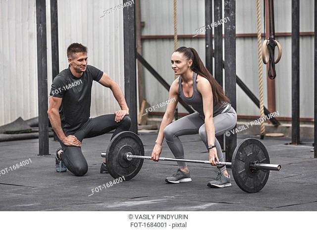 Male instructor looking at female athlete lifting barbell during crossfit training
