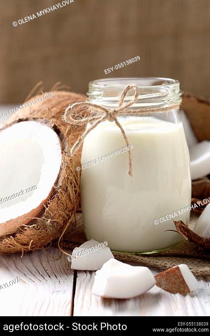 Mason jar of milk or yogurt on hemp napkin on white wooden table with coconut aside