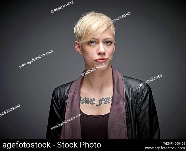 Portrait of blond young woman with tatoo in front of grey background