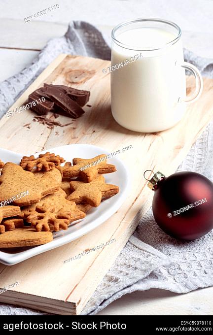 Close up with the traditional gingerbread cookies on a plate and a cup of milk on a wooden board on a kitchen towel