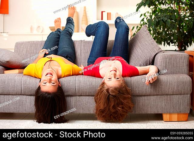 Teenage girls lying on couch upside down, looking at camera, smiling