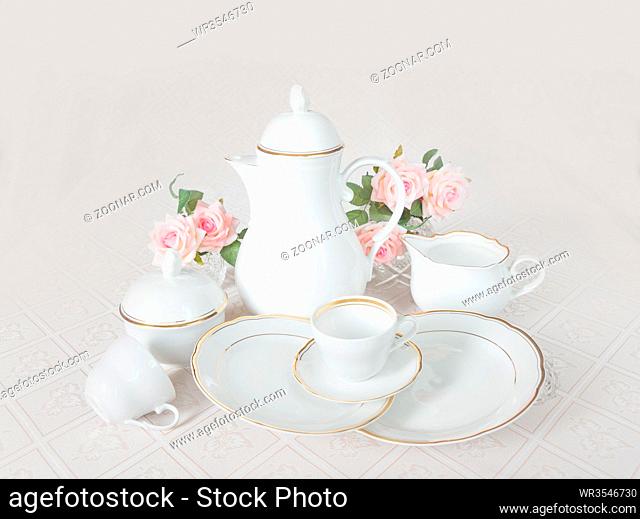 Classic white crockery for tea ore coffee: teapot, coffee pot, cup, serving plate, sugar bowl and creamer on a beautiful tablecloths