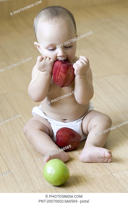 High angle view of a baby sitting on the hardwood floor and eating an apple