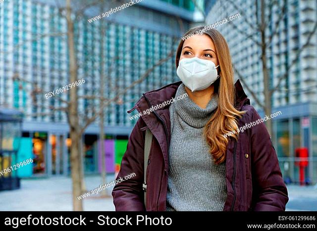 Medium shot of beautiful woman wearing protective face mask walking in city street in winter clothes