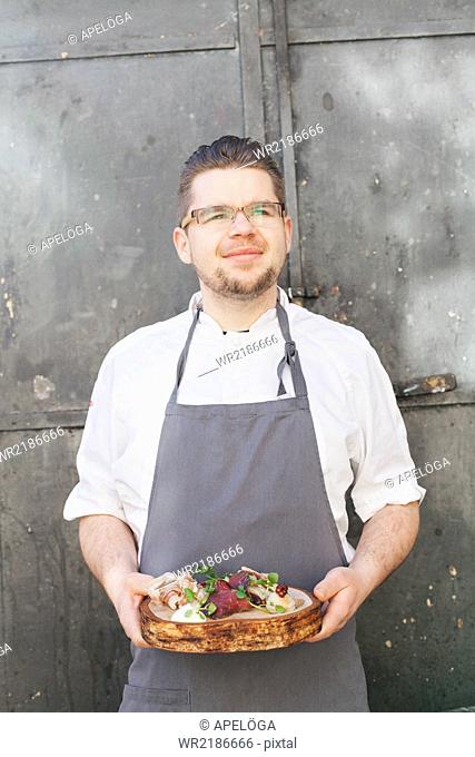Confident chef holding dish while looking away at outdoor cafe