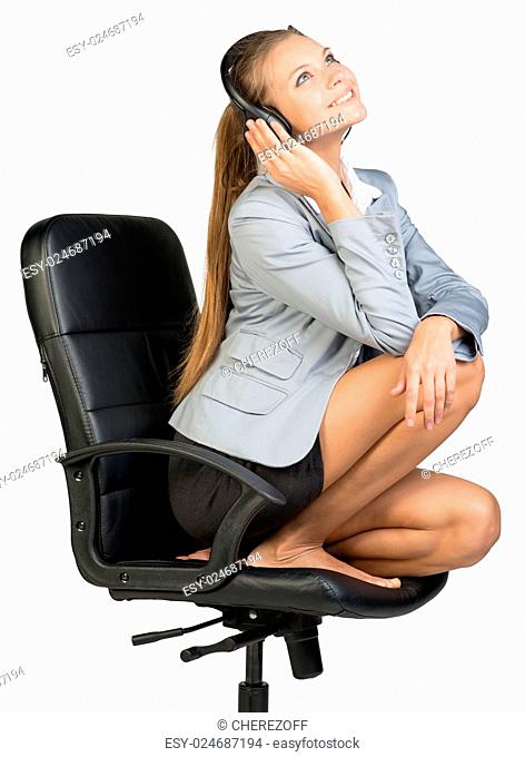 Businesswoman in headset sitting on office chair with legs, looking upwards, smiling. Isolated over white background