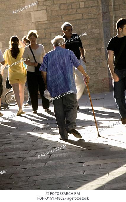 Old man with cane walks down crowded old section of Barcelona, Spain, in Barri Gotic area which is also known as the Gothic Quarter