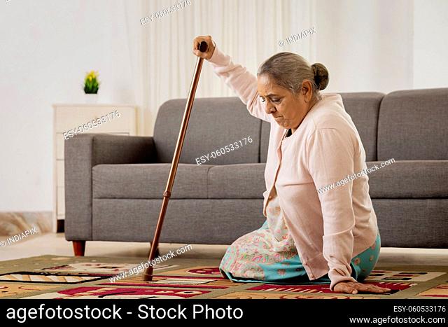 Old woman trying to stand with the help of walking stick