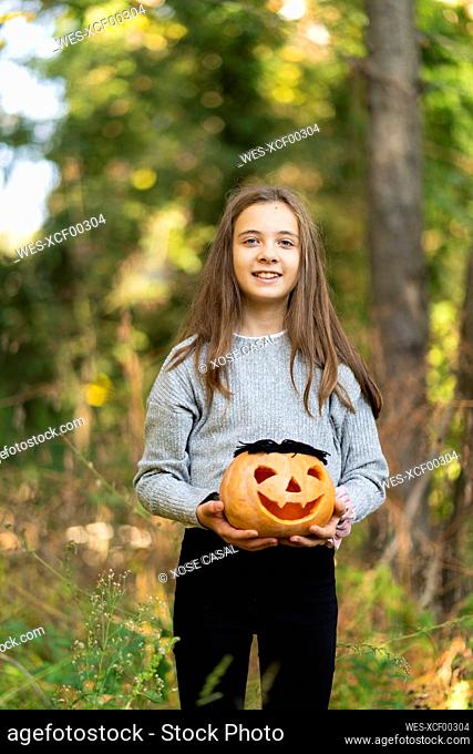 Smiling girl holding Halloween pumpkin while standing at park