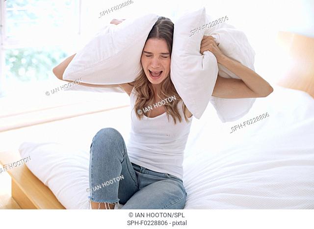 Young woman holding pillow over her ears and screaming