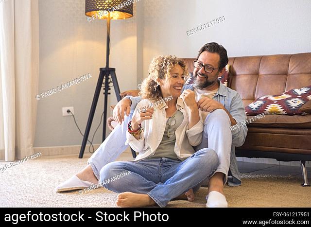 Adult young couple man and woman sitting on the floor at home enjoying in leisure indoor activity together - love and relationship middle age people having...