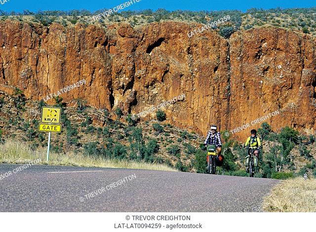Larapinta trail. Cyclists on road. Red sandstone cliffs