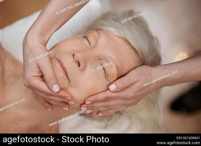 Face massage. A gray-haired woman looking relaxed while having face massage