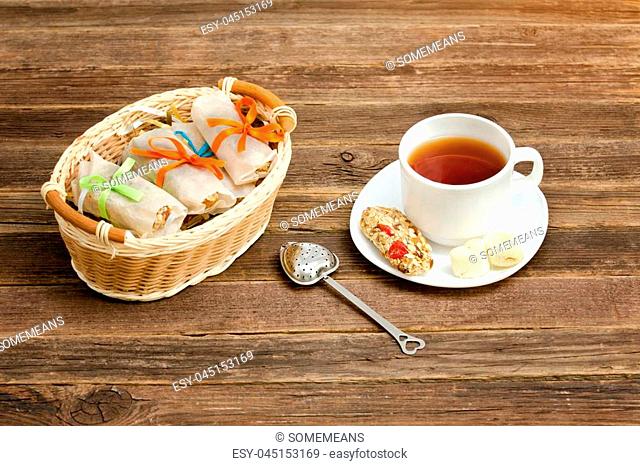 Mug of tea, muesli bars and tea strainer. Wicker basket with bars. Brown wooden background