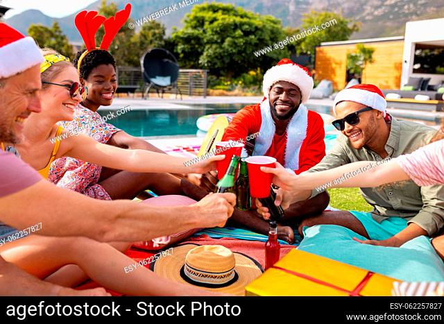 Happy diverse friends with santa hats having picnic in garden at christmas